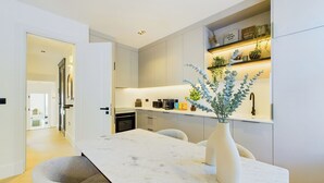 Een moderne keuken met een marmeren aanrechtblad, een vaas met groen en een inbouwkastje met keukenspullen.