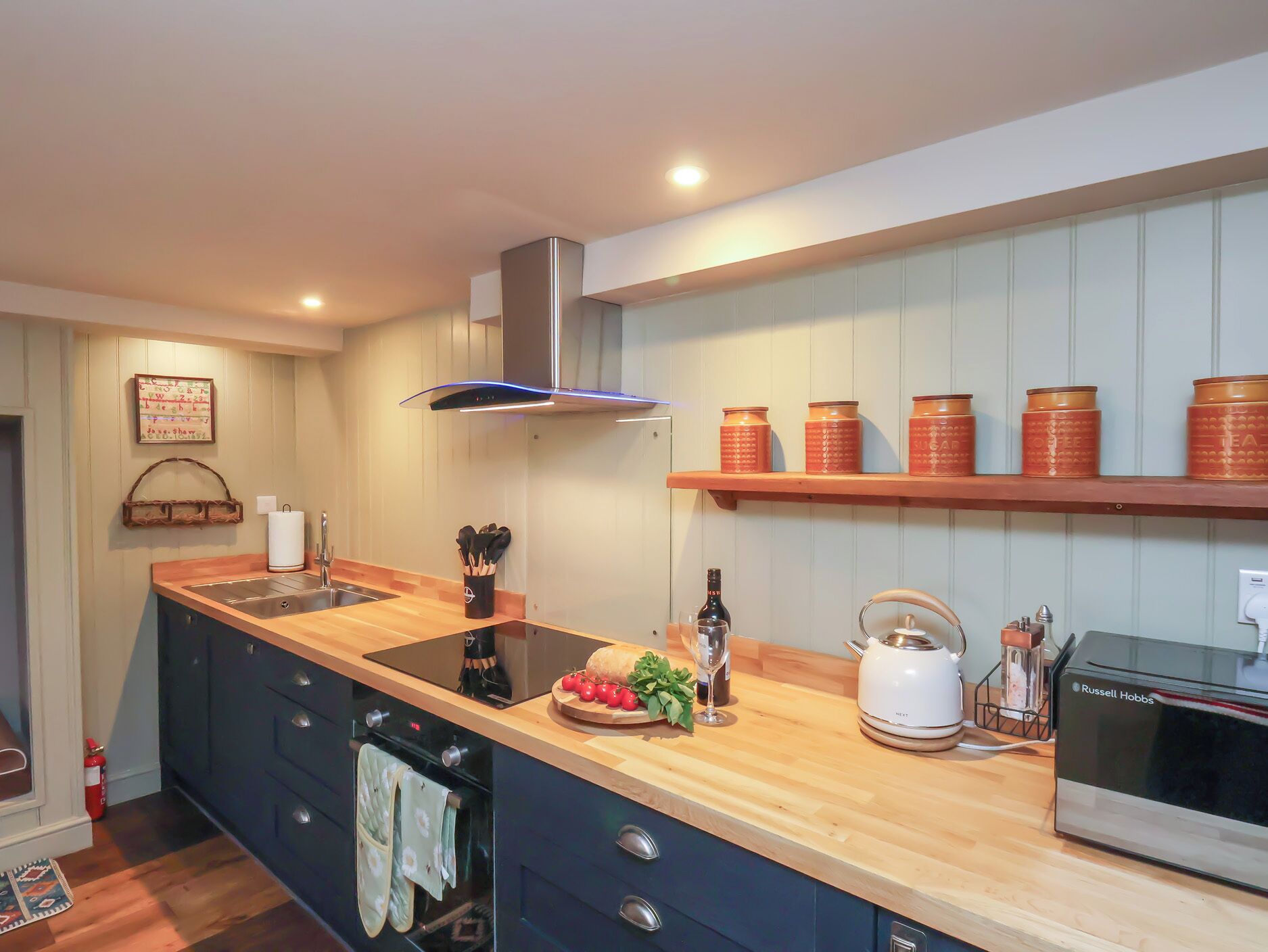 Una cocina moderna con encimera de madera, horno empotrado, hervidor y cafetera.