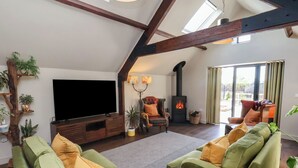 A spacious living room with a large flat-screen TV, comfortable green sofas, a wooden entertainment unit, a fireplace, and a view of the outdoors through a large window. - A Stones Throw (Scarborough)