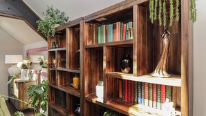 A wooden bookshelf with books, decorative items, and hanging plants. - A Stones Throw (Scarborough)