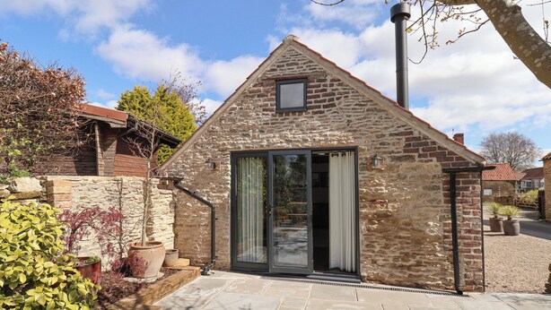 A stone cottage with a tiled patio, a glass door, and a small window. - A Stones Throw (Scarborough)
