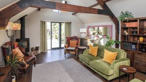 A spacious loft with exposed wooden beams, a green sofa with yellow pillows, a leather armchair, and a wooden bookshelf. - A Stones Throw (Scarborough)