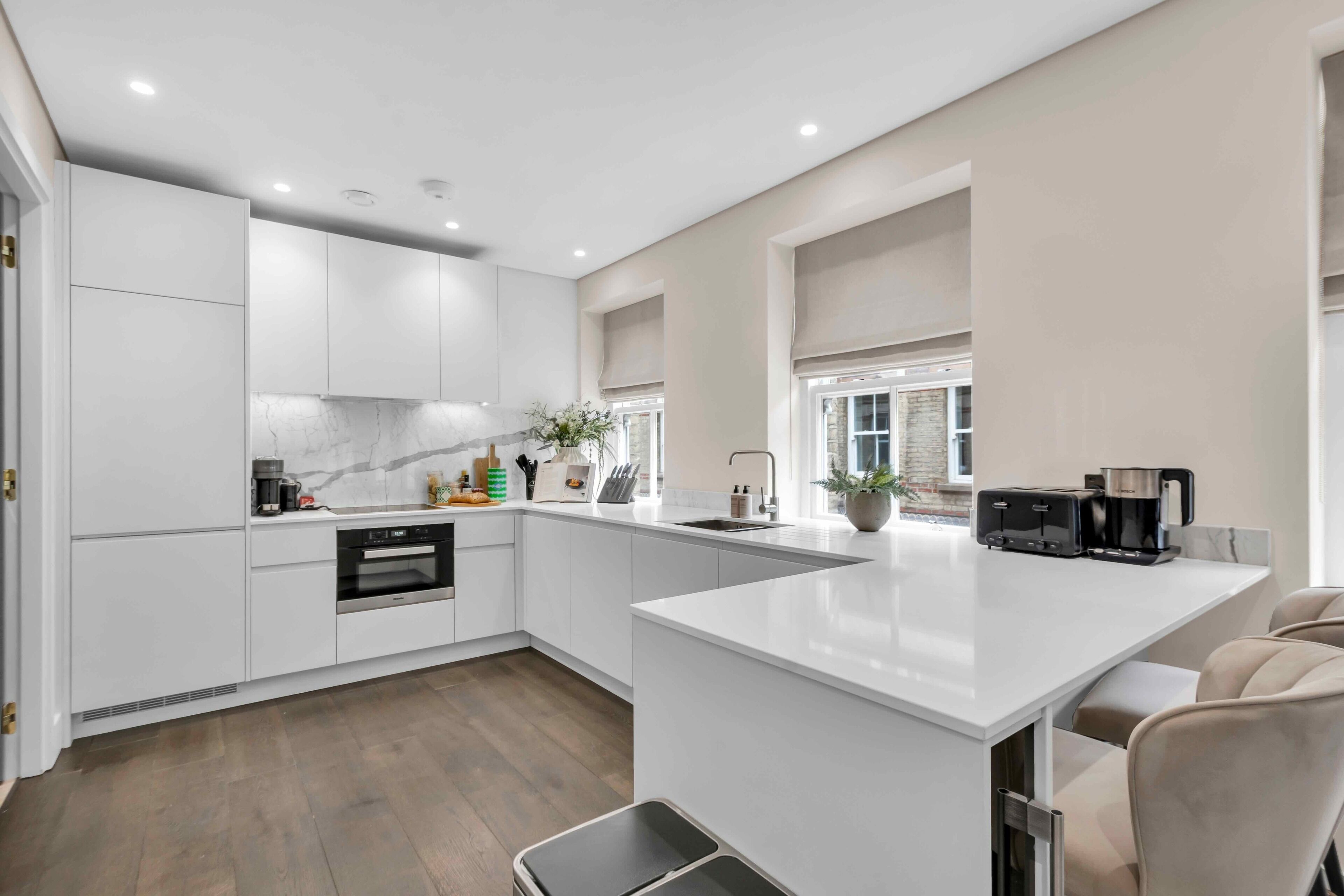 A modern kitchen with white cabinetry, a marble backsplash, and a large island with a sink and toaster.
