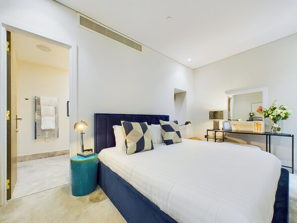 Un dormitorio moderno con una cama grande, mesitas de noche, un espejo y una puerta que da a otra habitación.