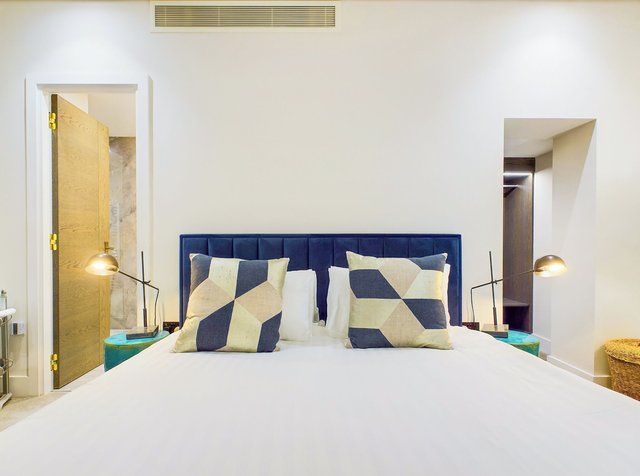 A bedroom with a large bed, two bedside lamps, and a wooden door.