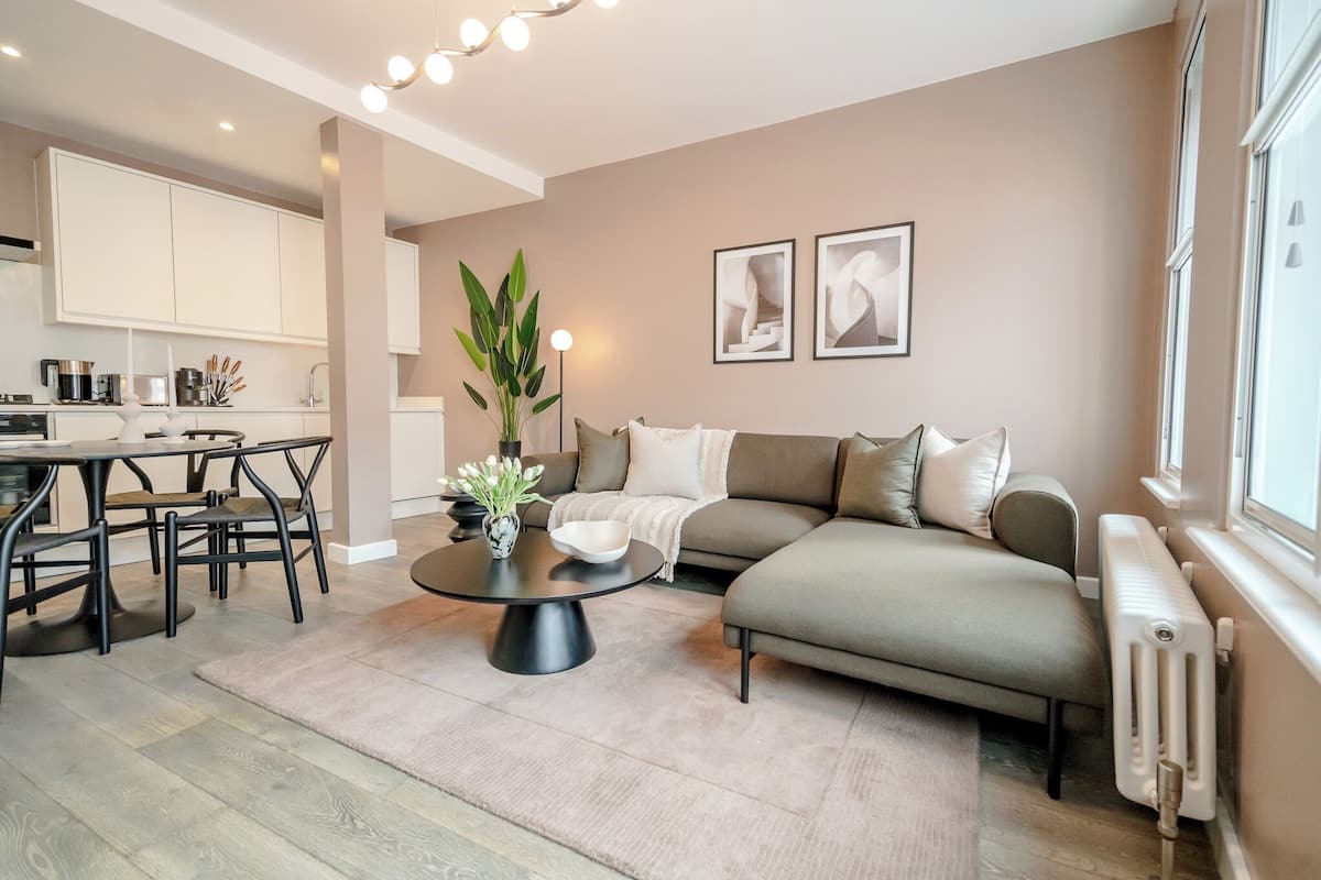 A modern living room with a sofa, coffee table, and dining area. There is a plant on the coffee table and artwork on the wall.