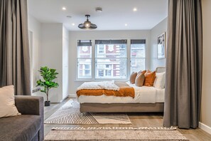 Een moderne slaapkamer met een groot bed, een kamerplant en uitzicht op de stad door grote ramen.