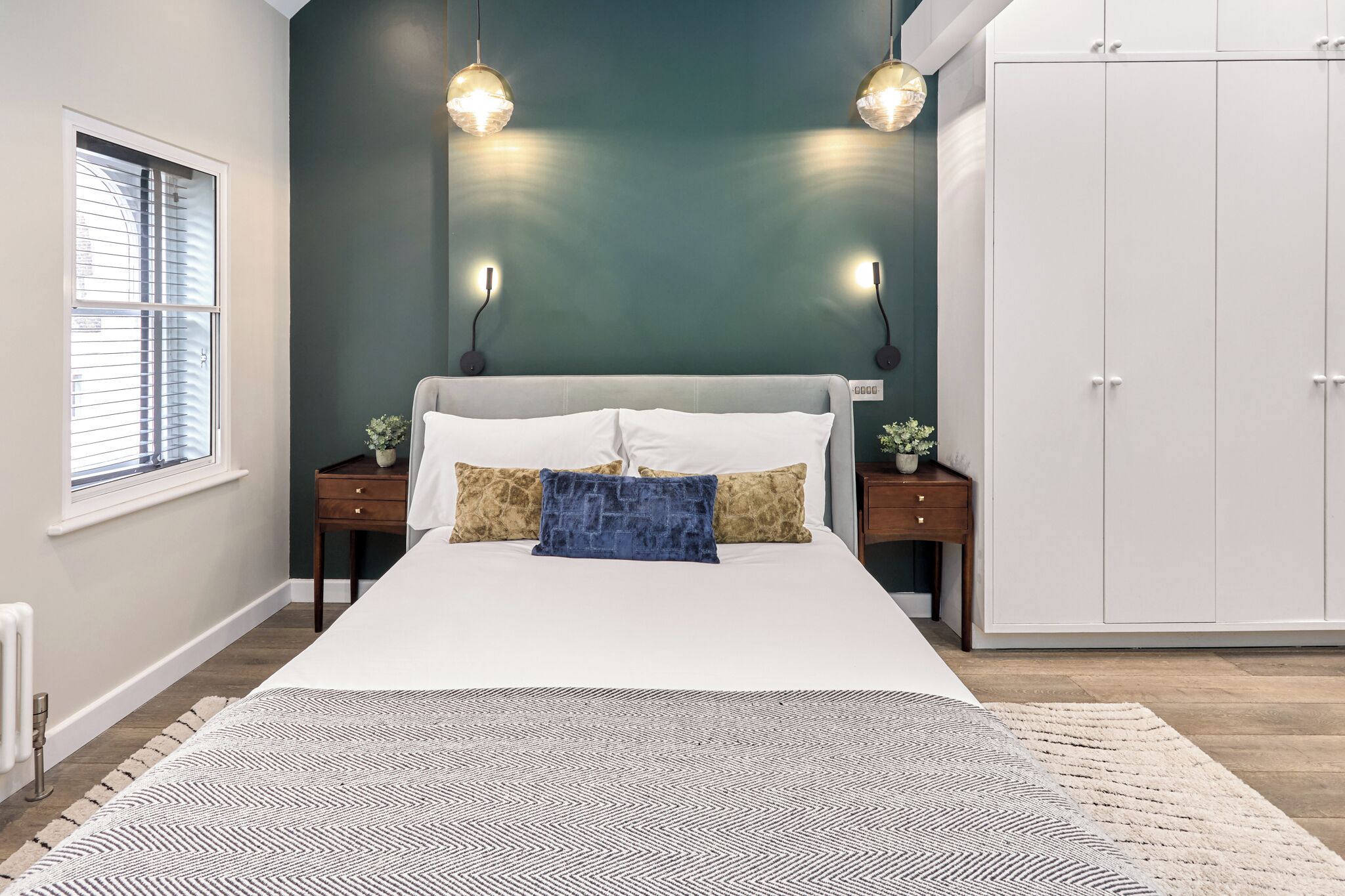 A bedroom with a bed, two bedside tables, a wardrobe, and pendant lights.