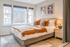 A bedroom with a large bed, a bedside table with a lamp, and two framed pictures on the wall. - Be London - The Chinatown Residences (London)
