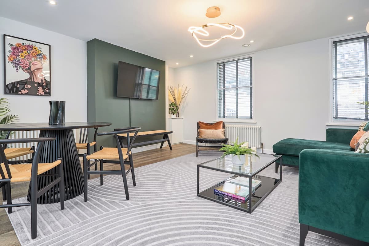A modern living room with a round table, chairs, a sofa, a coffee table, and a TV mounted on the wall.