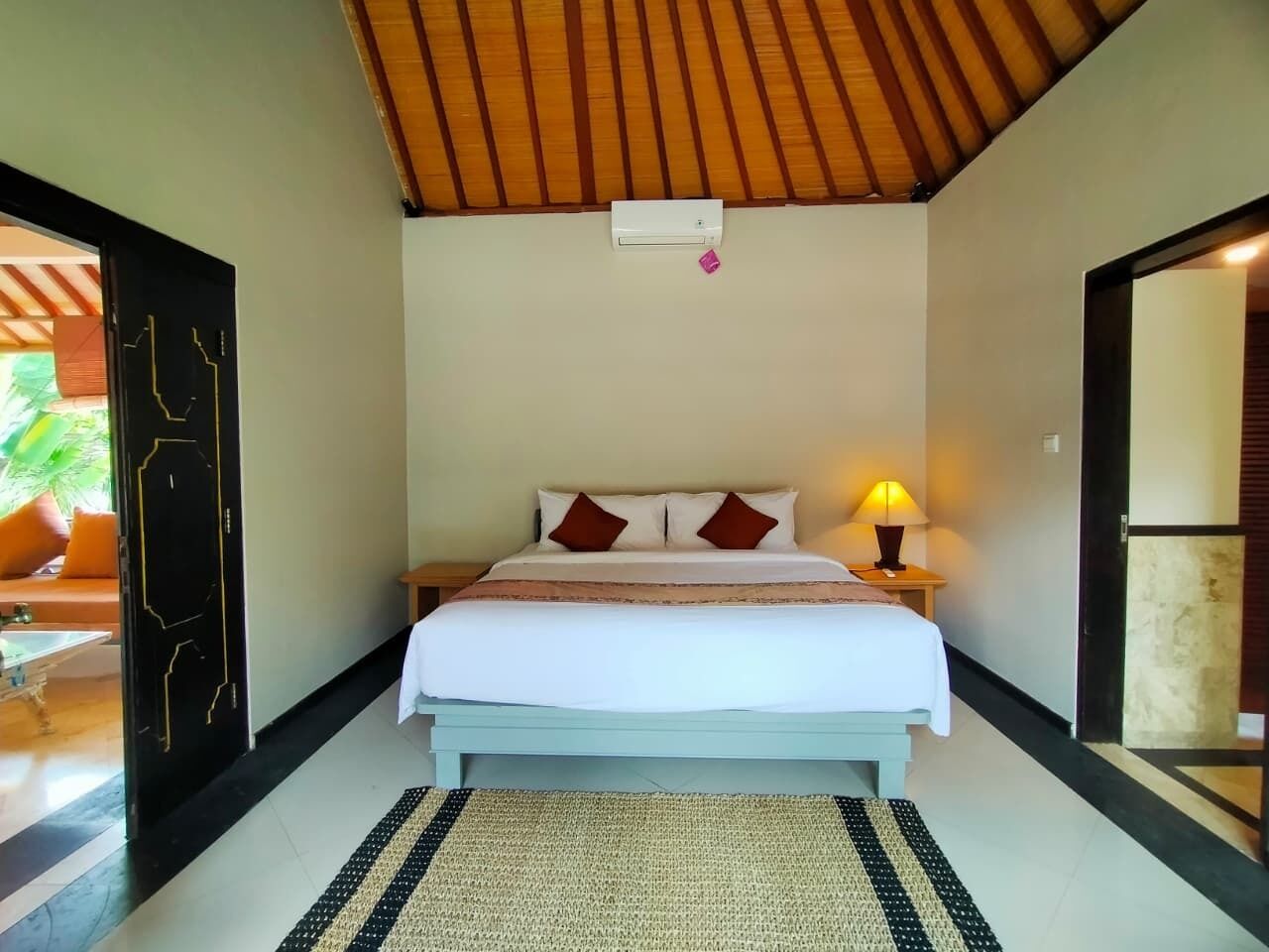 A bedroom with a bed, bedside lamp, and a view of the outside.