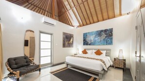 A bedroom with a bed, a sofa, a mirror, and artwork on the wall. - Dampati Villas (Denpasar)