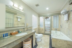 Een badkamer met een grote spiegel, twee wasbakken, een toilet en een bad.