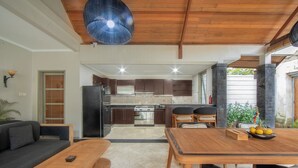 A modern kitchen with a central island, a dining area with a wooden table and chairs, and a cozy seating area with a sofa and a bench. - Dampati Villas (Denpasar)