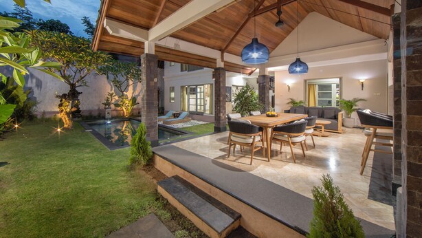 A spacious patio with a pool, outdoor seating, and a wooden ceiling structure. - Dampati Villas (Denpasar)