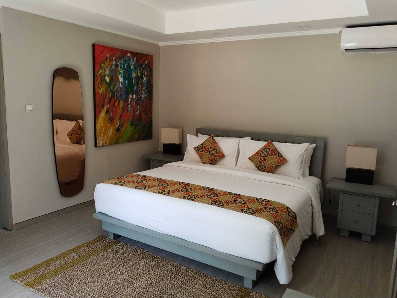 Une chambre moderne avec un grand lit, deux tables de chevet, une commode, un tableau et un miroir au mur.