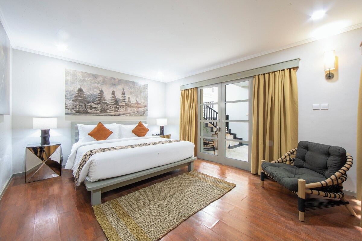 Een slaapkamer met een bed, een stoel, een schilderij en uitzicht op een trap.