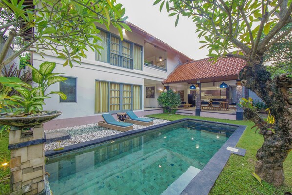 Une maison à deux étages avec une piscine, un espace salon extérieur et un jardin.