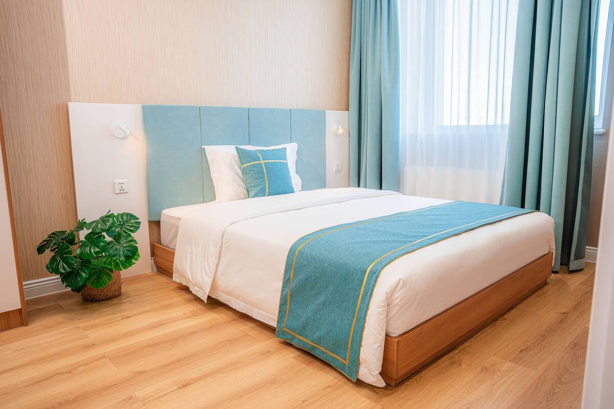A neatly made bed with a blue and white bedspread, a wooden headboard, and a potted plant beside the bed.