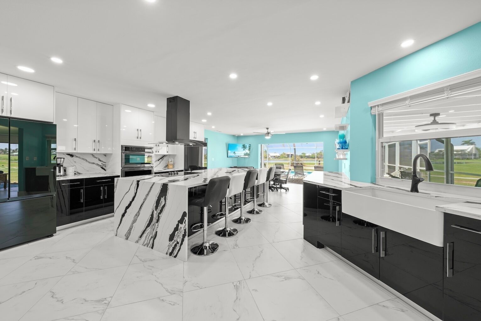 A modern kitchen with a marble island, black cabinets, and a view of the outdoors.