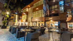 An outdoor dining area with multiple tables and chairs, a modern building with large windows, and a decorative metal fence. - GRANDEUR SANCHI RESORT (Calangute)