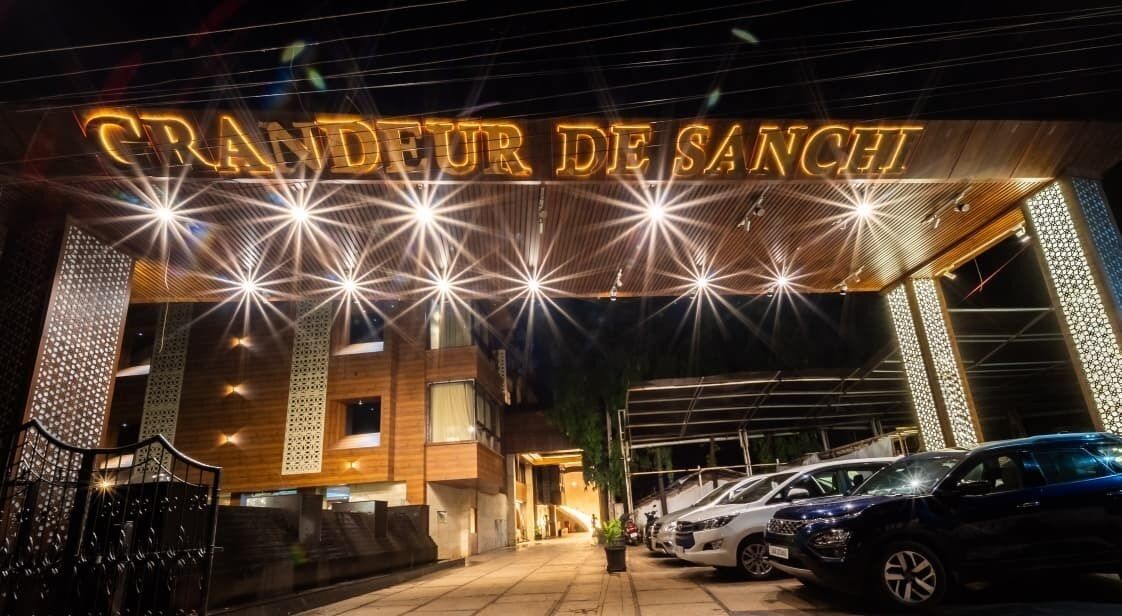 Entrada de un hotel con un llamativo letrero iluminado que dice "GRANDEUR DE SANCHI".