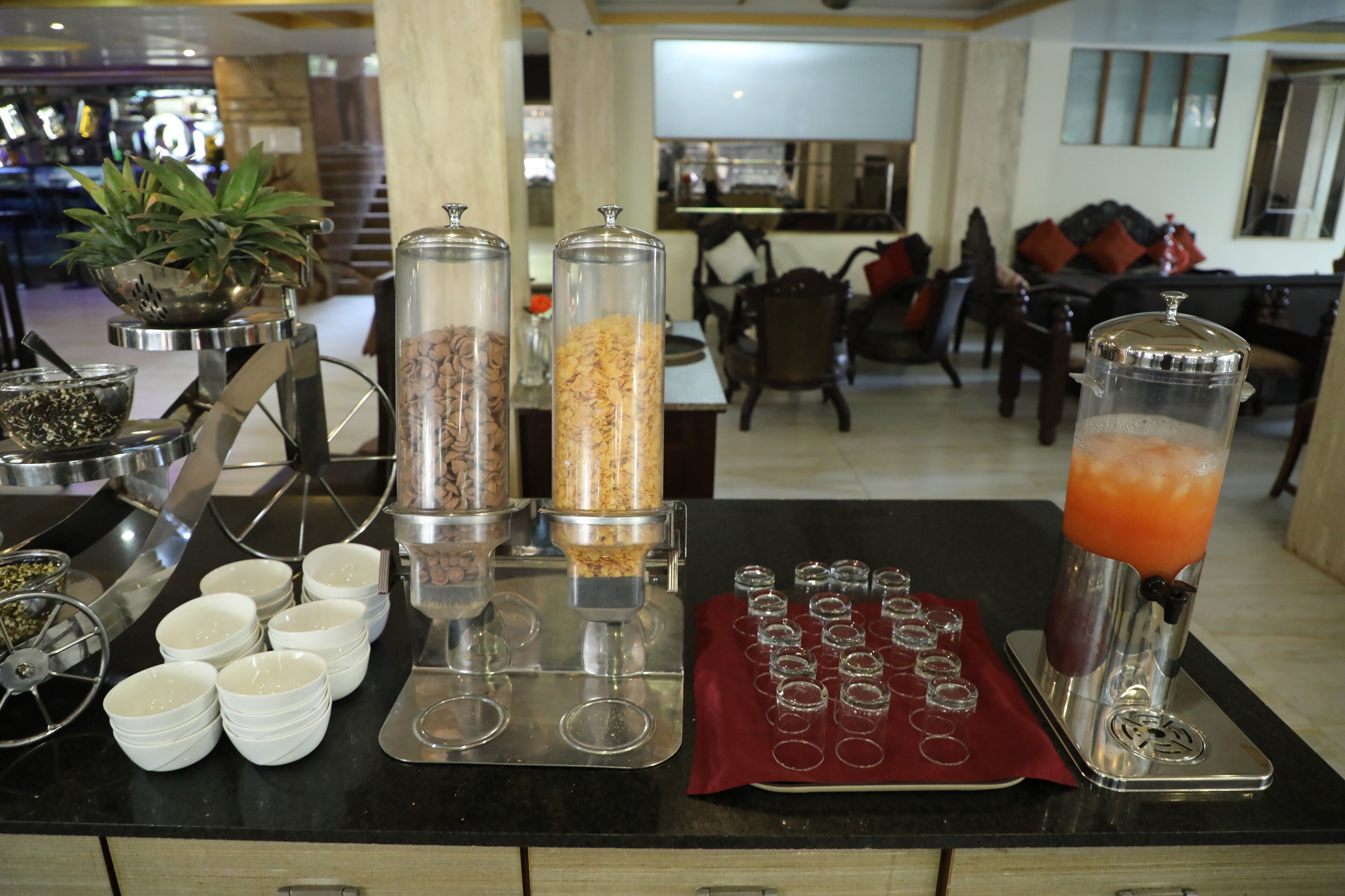 A buffet setup with various food dispensers, a fruit punch dispenser, and a tray of glasses.