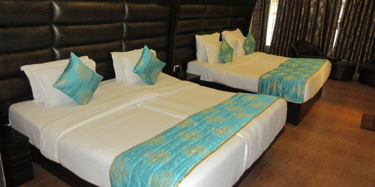 A hotel room with two beds, each with white linens and teal decorative pillows.