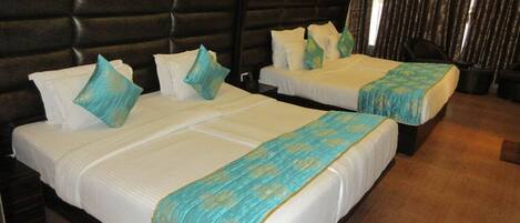 A hotel room with two beds, each with white linens and teal decorative pillows.