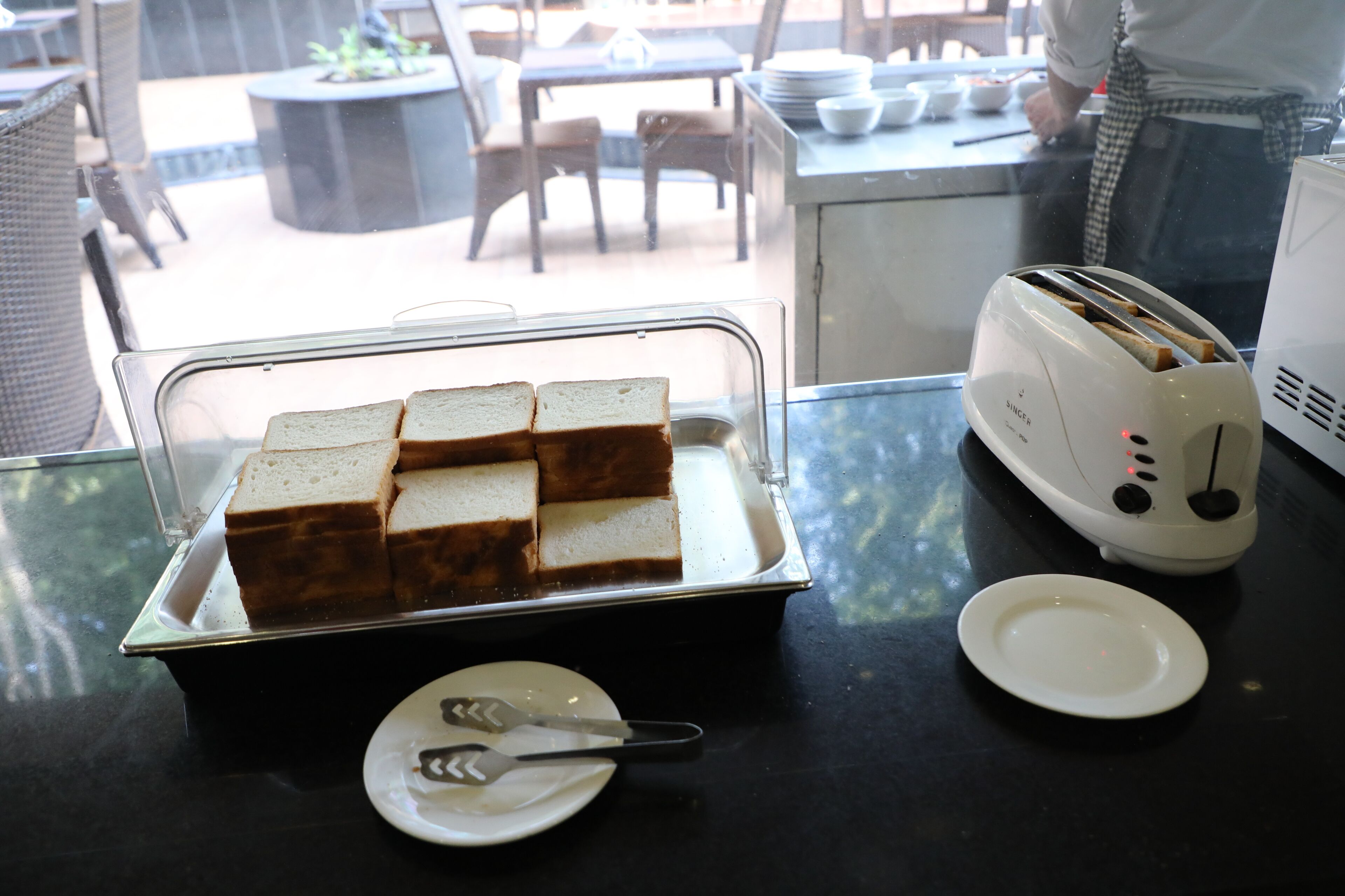 A breakfast setup with a toaster, a tray of bread, and a plate with utensils.