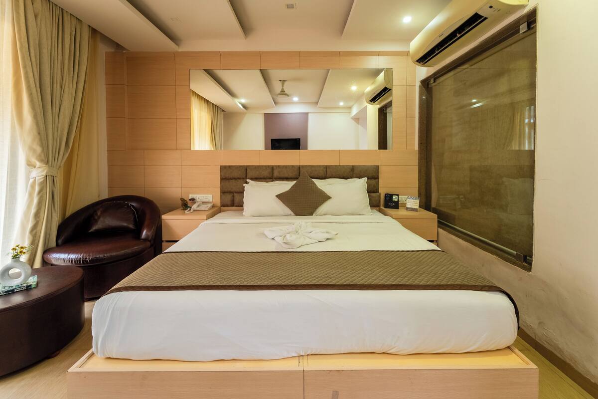 A hotel room with a large bed, a leather armchair, a bedside table, and a large window.