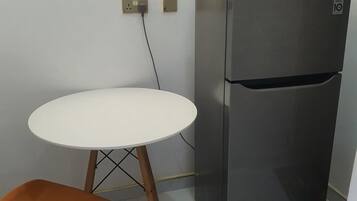 A compact kitchen with a white table and a modern stainless steel refrigerator.