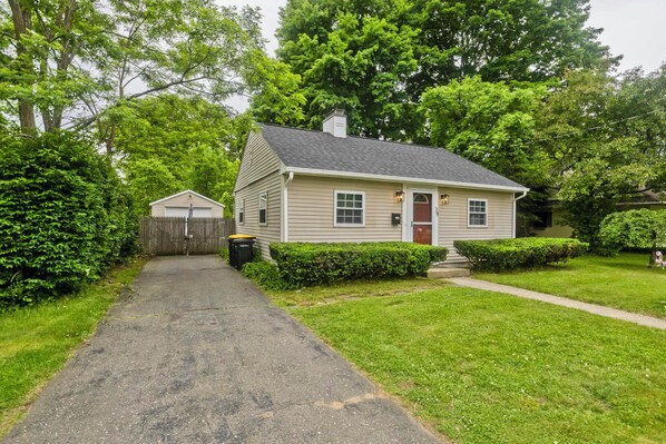 A single-story house with a front door, a small attached garage, and a pathway leading to the door. - Updated 2 BR Cozy Cottage in lovely Longmeadow with fenced yard & AC. (Longmeadow)