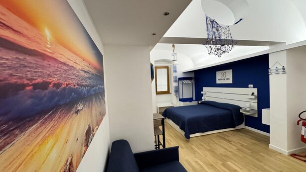 A modern bedroom with a large ocean sunset mural, a bed, a desk, and a hanging light fixture.