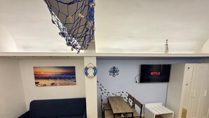 A cozy living space with a blue sofa, a wooden dining table, and a TV displaying Netflix.