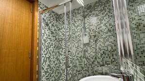 A bathroom with a shower, a sink with a vase of toiletries, and a tiled floor.