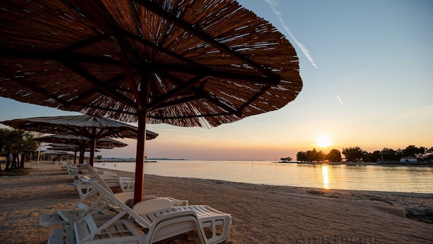 A beach with lounge chairs and thatched umbrellas. - Apartments Ivankovic (Nin)