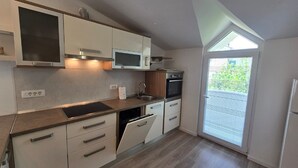 A modern kitchen with white cabinets, a microwave, an oven, and a dishwasher. There is a window providing natural light and a view of greenery outside. - Apartments Ivankovic (Nin)