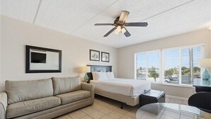 A hotel room with a bed, a sofa, a small table, and a ceiling fan. - Beacher's Lodge Studio Suite (not directly oceanfront) (Saint Augustine)