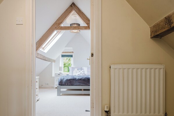 Une chambre avec un plafond en pente, un lit, un radiateur et une fenêtre.