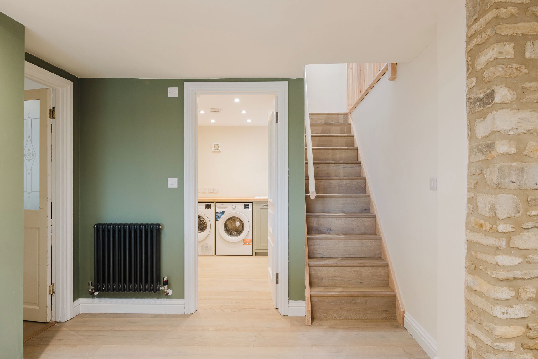 Un couloir avec un radiateur, un escalier et, au fond, un espace dédié à la buanderie.
