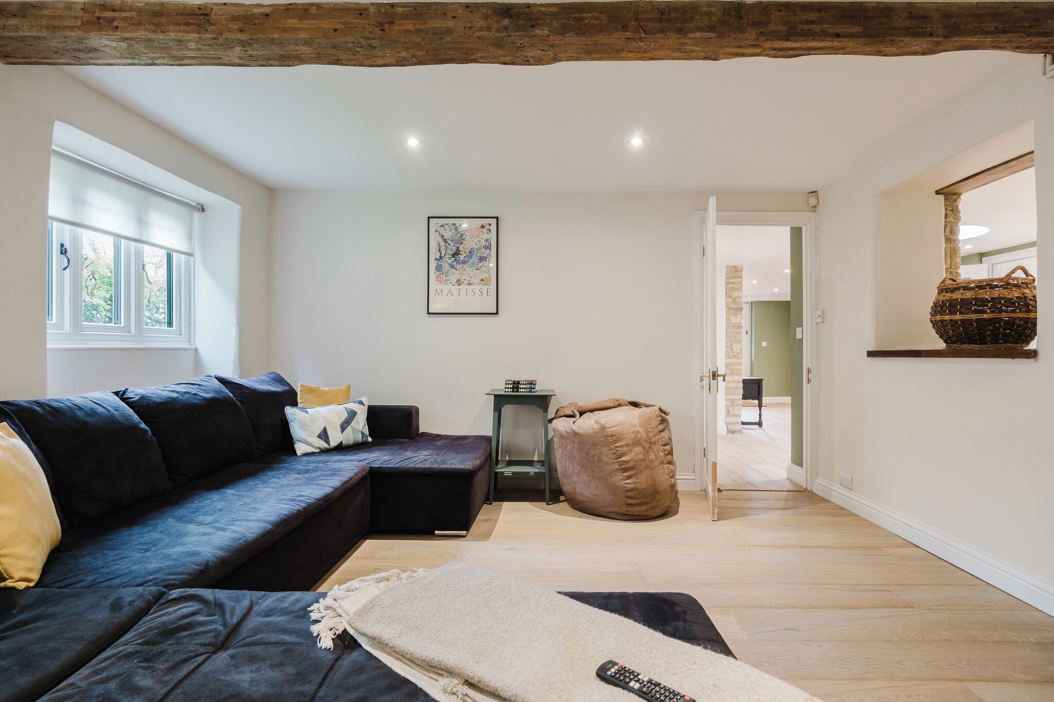 Un salon moderne avec un canapé de couleur foncée, un fauteuil en forme de poire, une œuvre d’art encadrée accrochée au mur et un panier posé sur une étagère.
