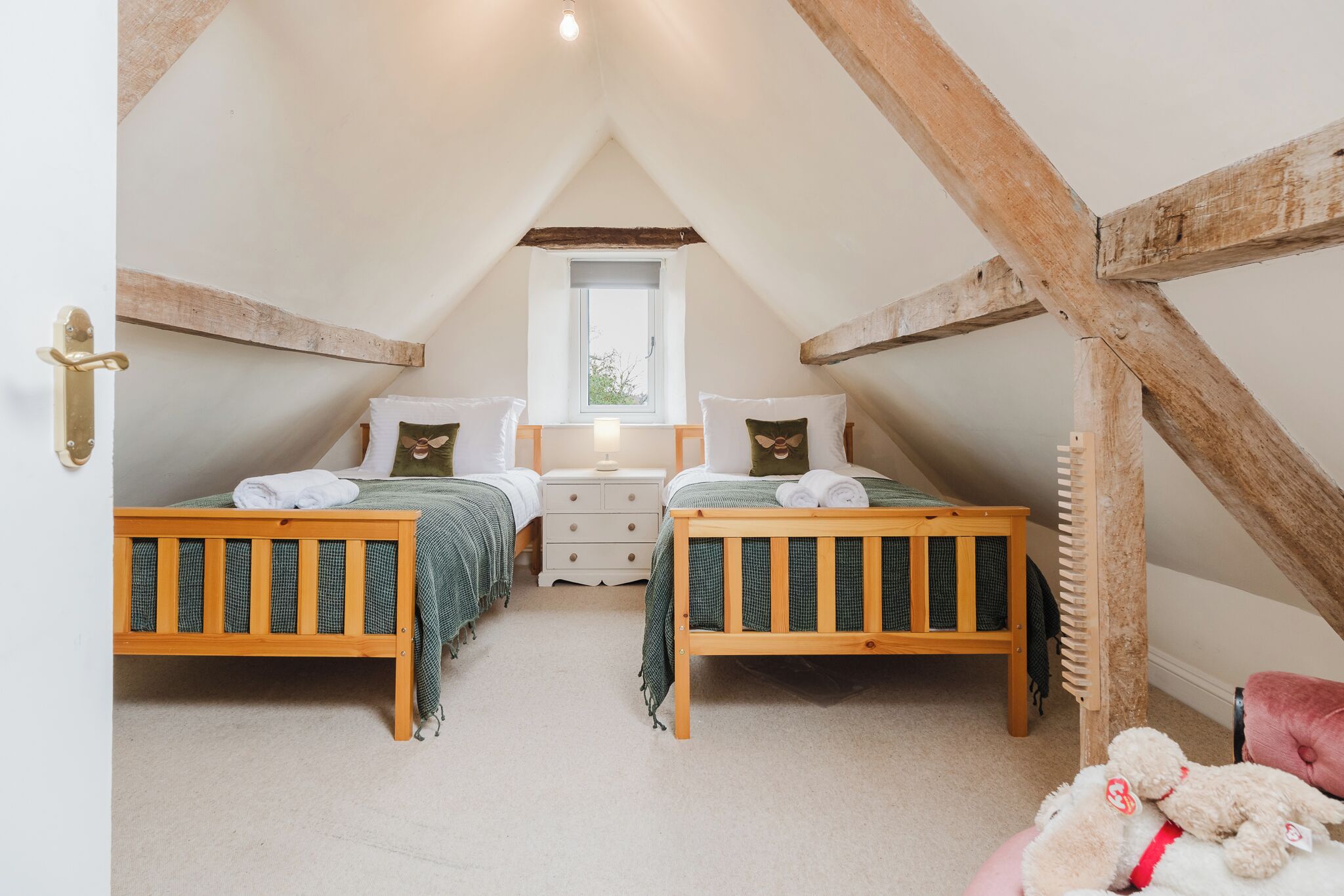 Une chambre mansardée chaleureuse avec deux lits en bois, une petite fenêtre et une structure de poutres apparentes en bois au plafond.