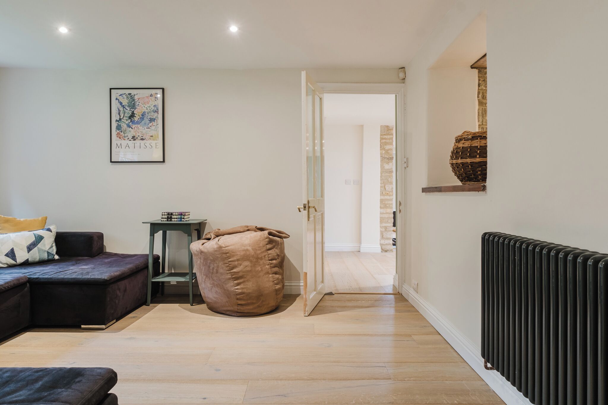 A modern living room with a sectional sofa, a bean bag chair, a framed artwork, and a radiator.