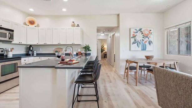 A modern kitchen with a central island, bar stools, a dining area with a table and chairs, and a painting on the wall. - Panorama View - Mountain Views - Community Pool (Fountain Hills)