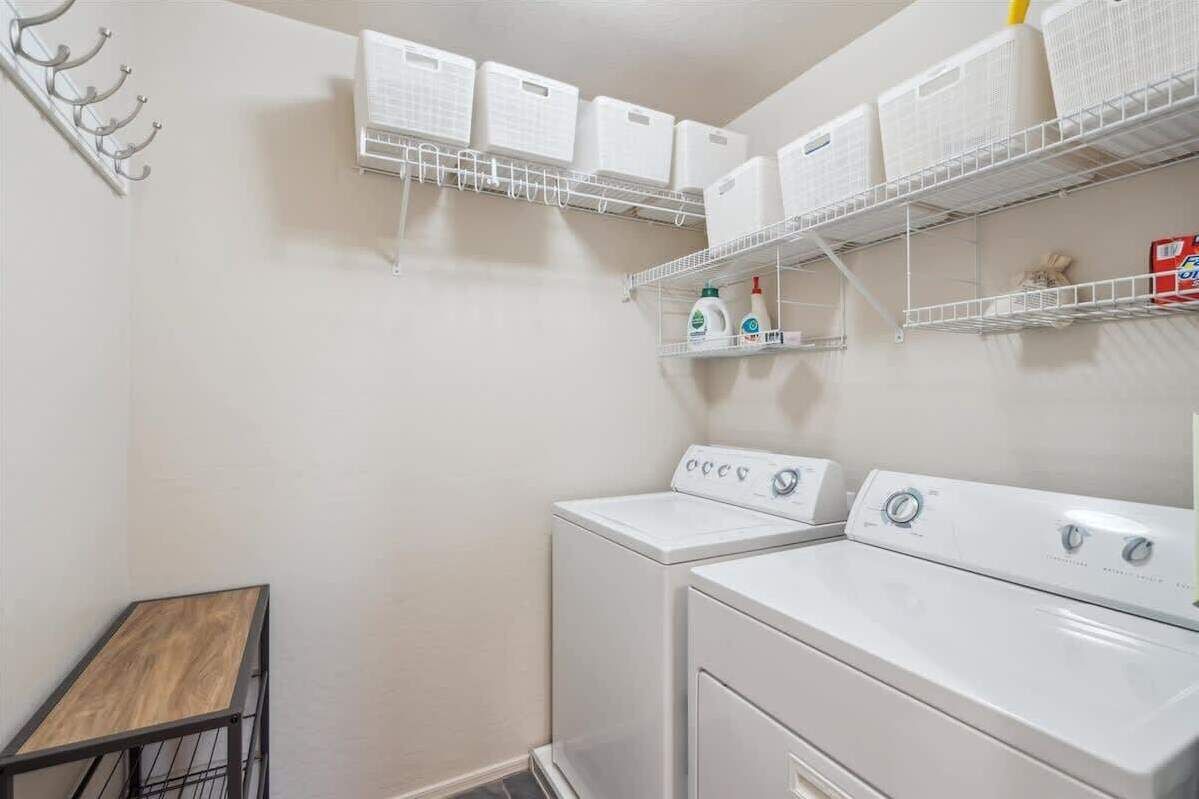 A laundry room with two stacked washing machines, a drying rack, and storage shelves above.