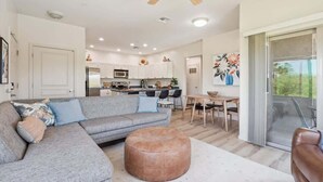 A modern living room with a grey sofa, a brown ottoman, and a dining area with a table and chairs. - Panorama View - Mountain Views - Community Pool (Fountain Hills)