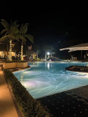 A nighttime swimming pool area with palm trees, a water slide, and a covered seating area. - Charming deluxe room in 5-star hotel in Nai Harn with gym and kids water park (Tambon Rawai)