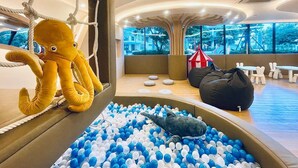Una habitación con piscina de bolas, un peluche de pulpo y un sillón de ganchillo.