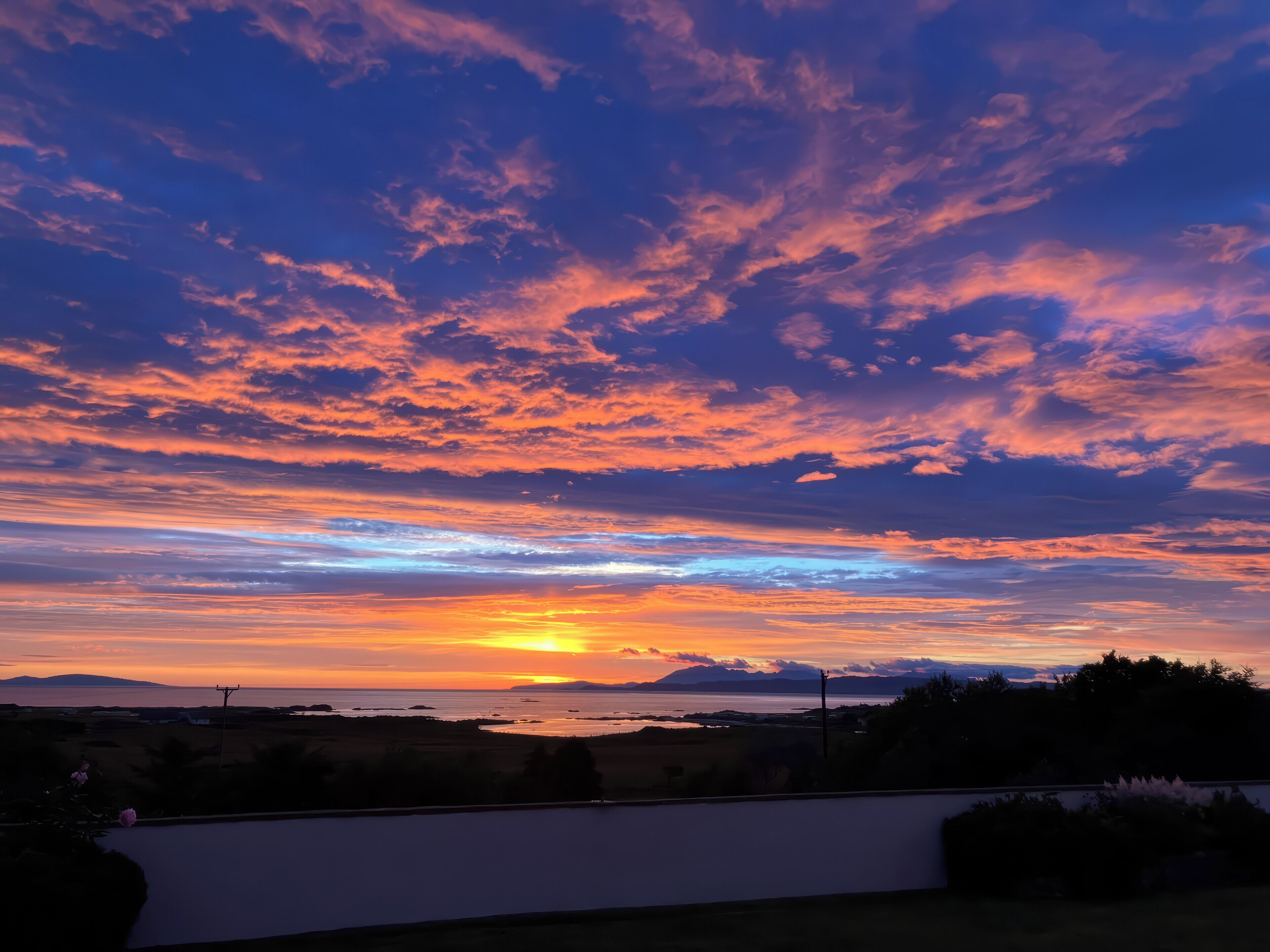 A sunset over a coastal landscape with a clear sky and distant mountains.